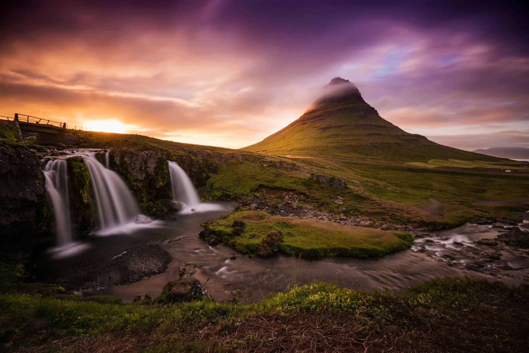 Hinter dem Vulkan Kirkjufell auf Island scheint die Mitternachtssonne hervor, wie sie zu Mittsommer gut zu sehen ist.