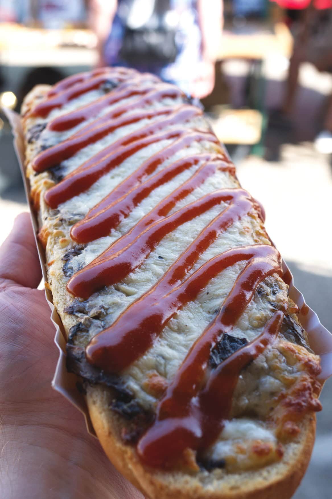 Eine Hand hält eine überbackene und mit Ketchup garnierte Baguettehälfte