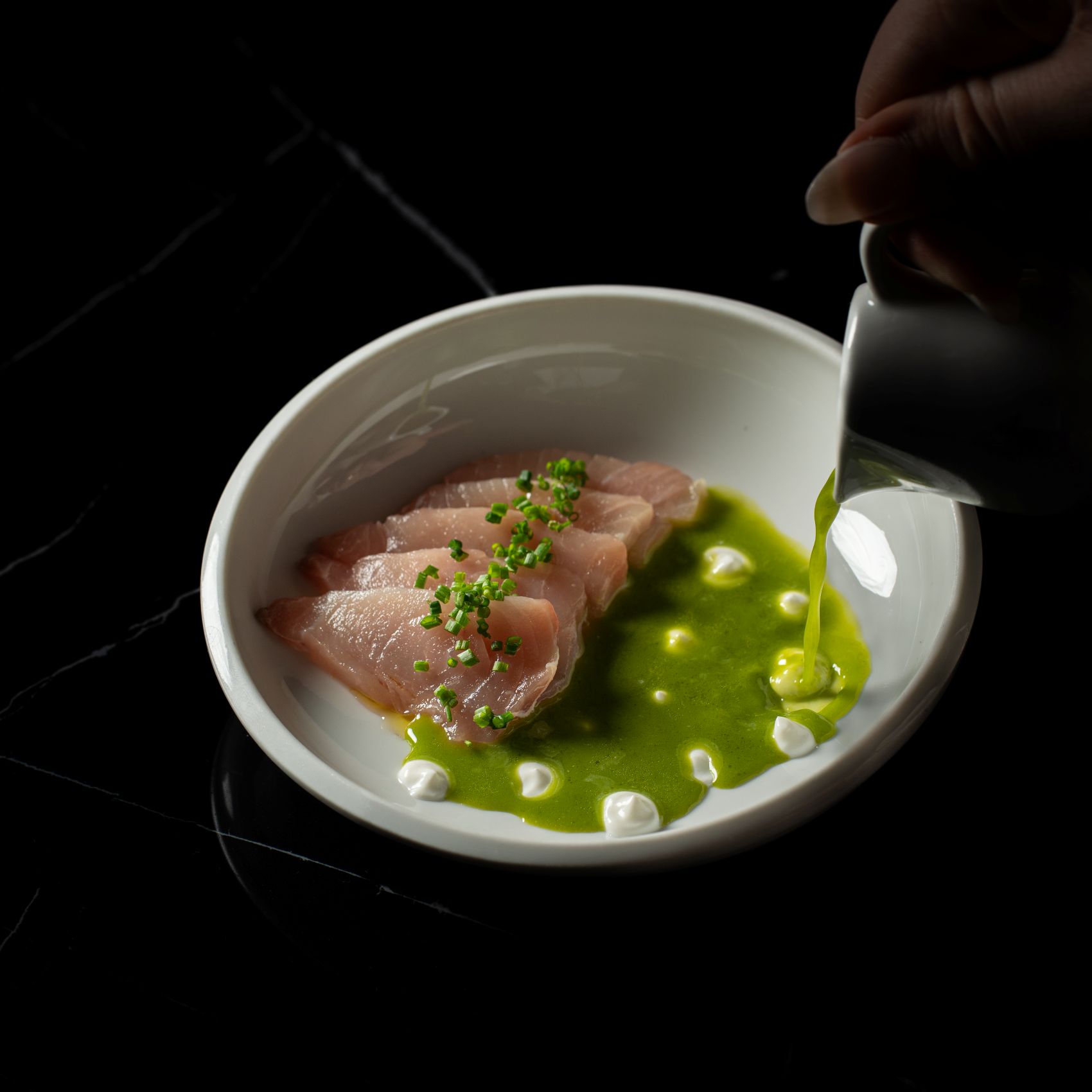 Fine Dining: Grüne Sauce wird auf rohem Fisch gegossen