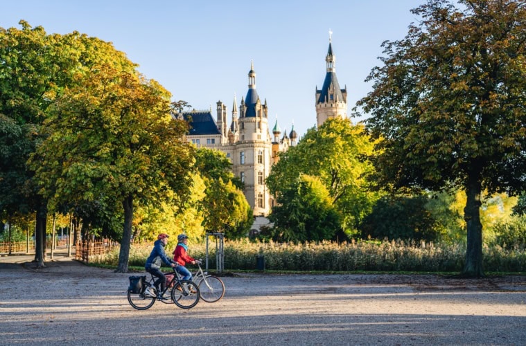 Zwei Fahrradfahrer fahren vorbei an Schweriner Schlösser.