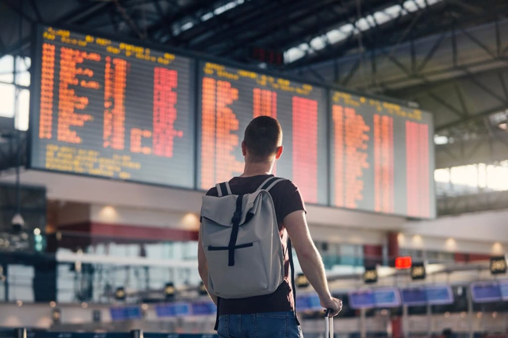 Junger Reisender am Flughafen blickt auf große Flug-Anzeigetafel
