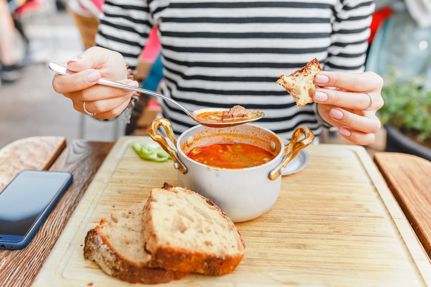 Frau ist aus einem Topf Gulaschsuppe mit Brot