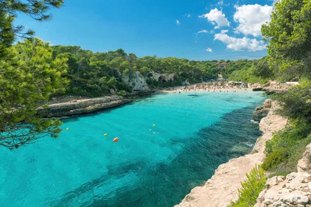 Eine paradiesische Bucht auf Mallorca mit türkisblauem Wasser, umgeben von hellem Sandstrand und dichtem, grünem Wald.