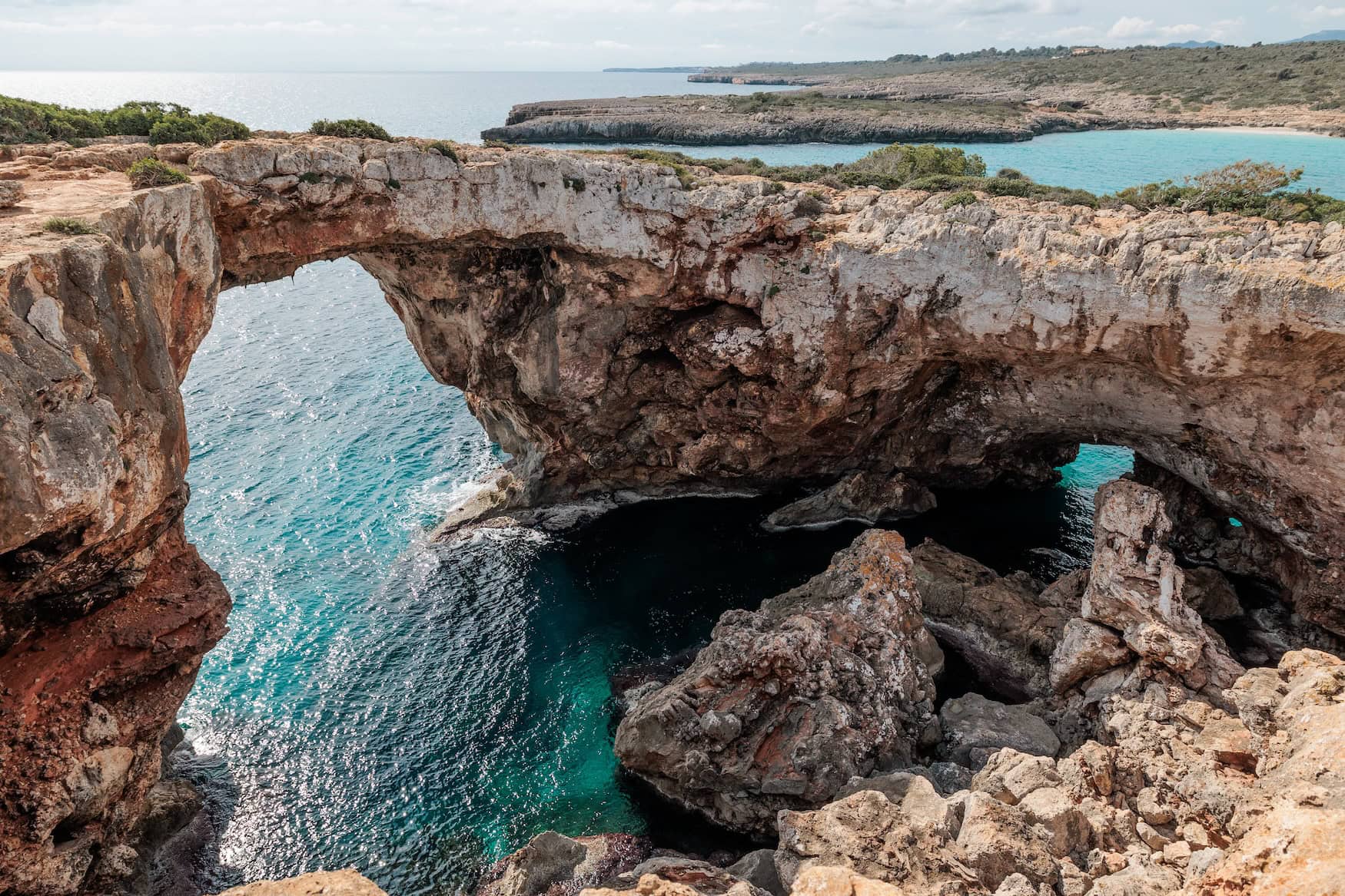 Die Cala Varques auf Mallorca; eine Felsenbrücke mit zwei Bögen, unter denen das blaue Wasser des Mittelmeers liegt