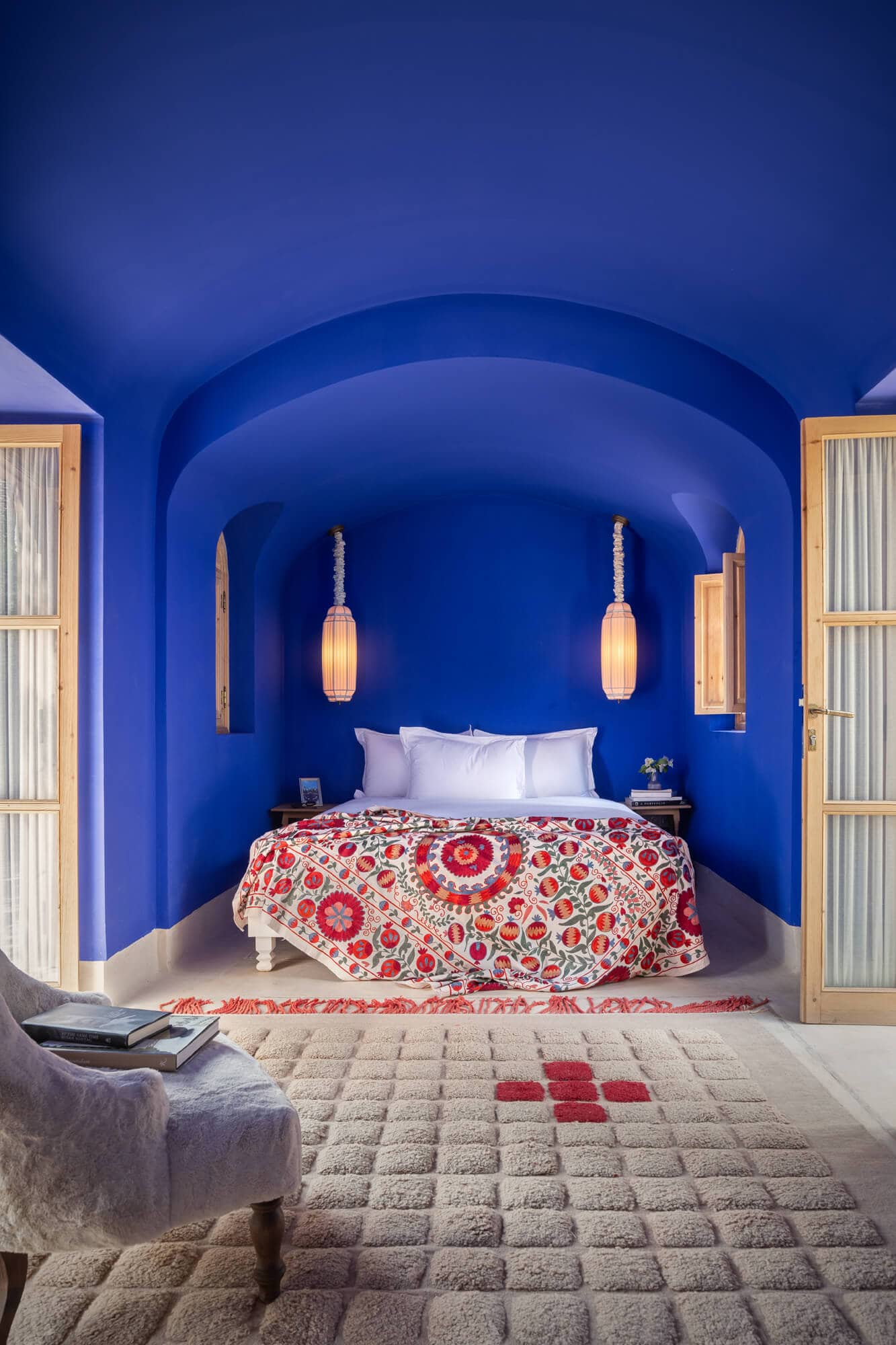 Hotelzimmer in Marrakesch, knallblau in der Mitte ein Bett mit einer rot gemusterten Decke, zwei offenen Terrassentüren