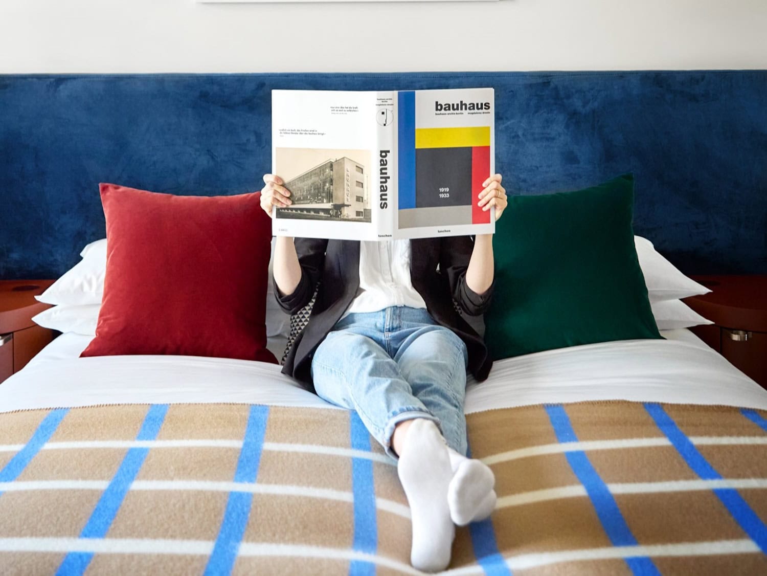 Hotelzimmer Kimpton Main Frankfurt, Mann auf Bett in bunten Farben mit Bauhaus-Buch vor dem Gesicht