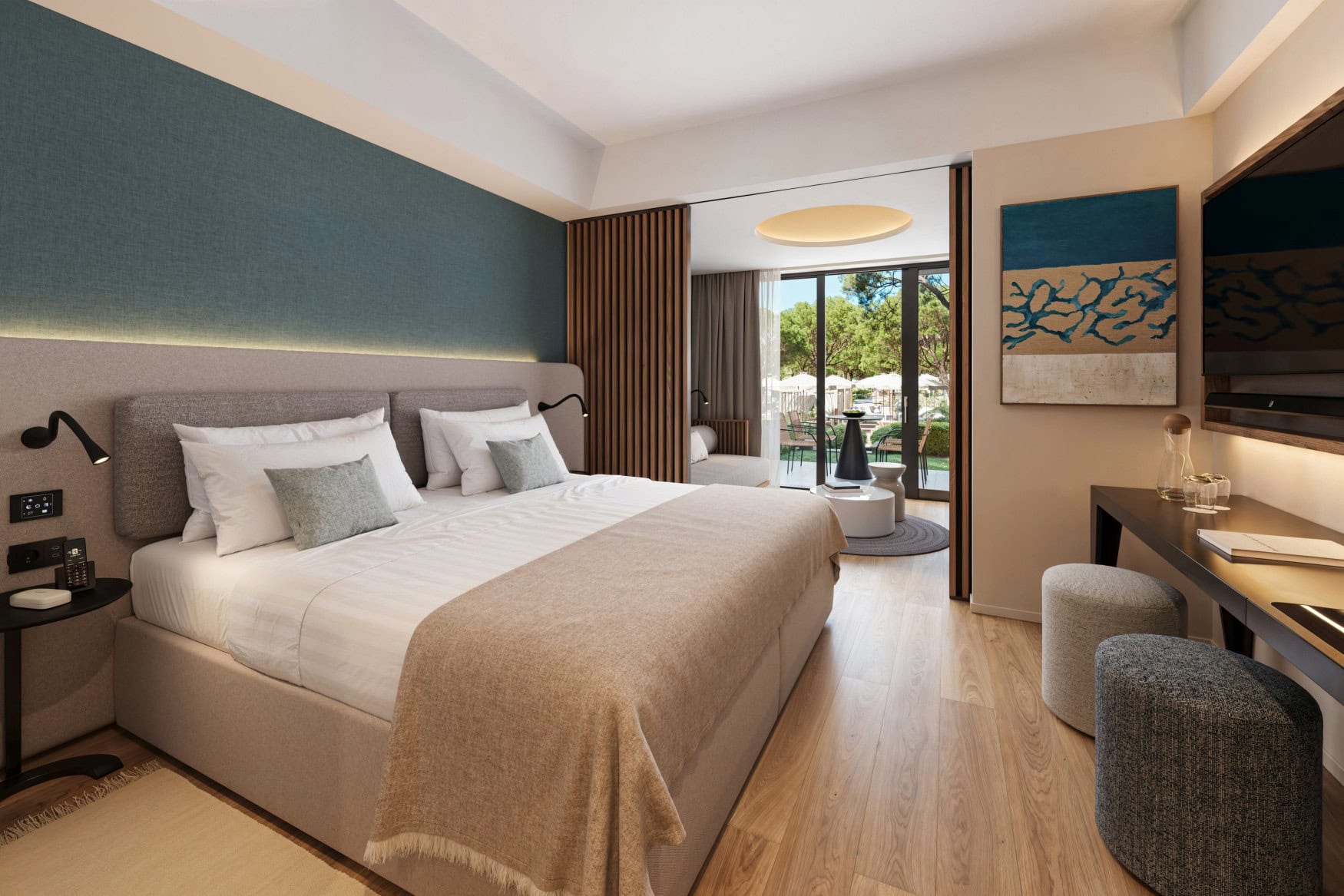 Ein Hotelzimmer mit hellem Holzboden, blauer Textilwand und einem zentralen, großen Doppelbett. Das graue Polsterbett ist mit weißen Laken bezogen. Rechts hinter dem Bett folgt ein Wohnbereich mit einer grauen Couchm dahinter ein hohes, bodentiefes Fenster, das per Tür zu einem begrünten Außenbereich führt.