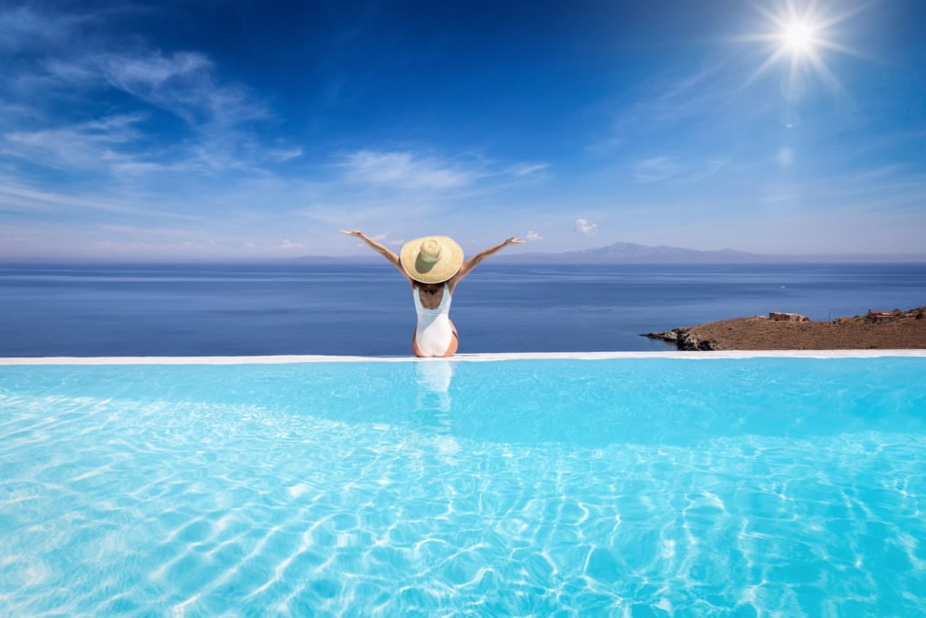 Eine Frau sitzt am Rand eines Pools und blick aufs Meer. Laut einer Umfrage gönnen sich immer mehr Leute im Urlaub Luxus!