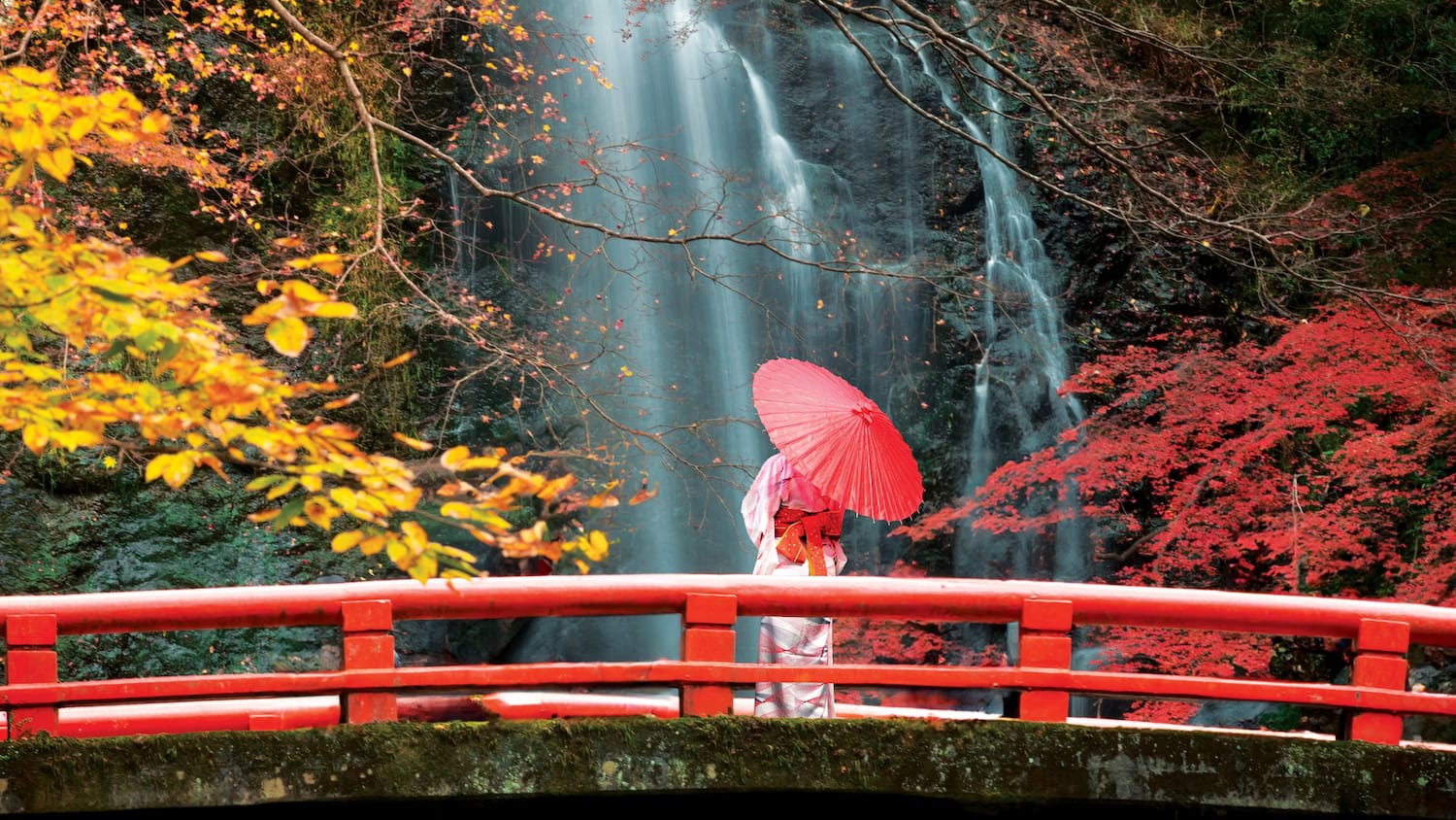 Frau in Japan auf einer Brücke vor einem Wasserfall