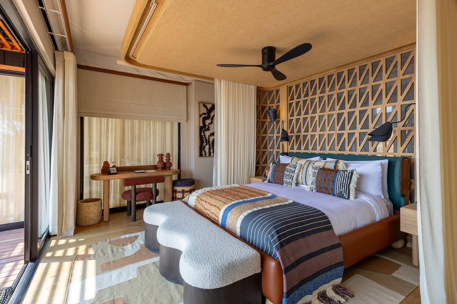 Anantara Kafue River Camp, Zimmer, großes Bett mit Blick aus dem Fenster, alles in Naturfarben mit afrikanisch-bunter Decke auf dem Bett.