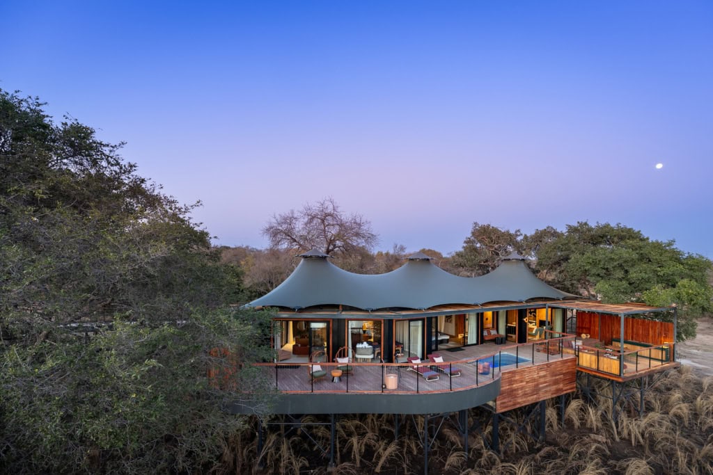 Anantara Kafue River Sambia : Gästevilla im lilafarbenen Sonnenuntergang mit großzügigem Außenbereich und kleinem Pool. Drumherum sind Bäume.