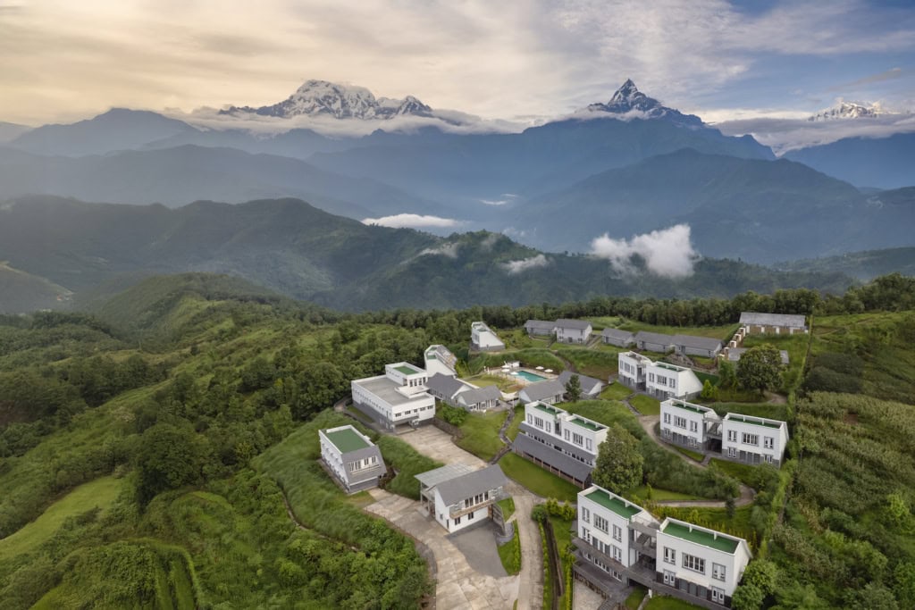 Himalayan Hideaway Resort Pokhara - Luftaufnahme, verschiedene Gebäude und Villen inmitten der Berglandschaft des Himalaya, viel Grün drum herum und in der Ferne das Annapurna Massiv.