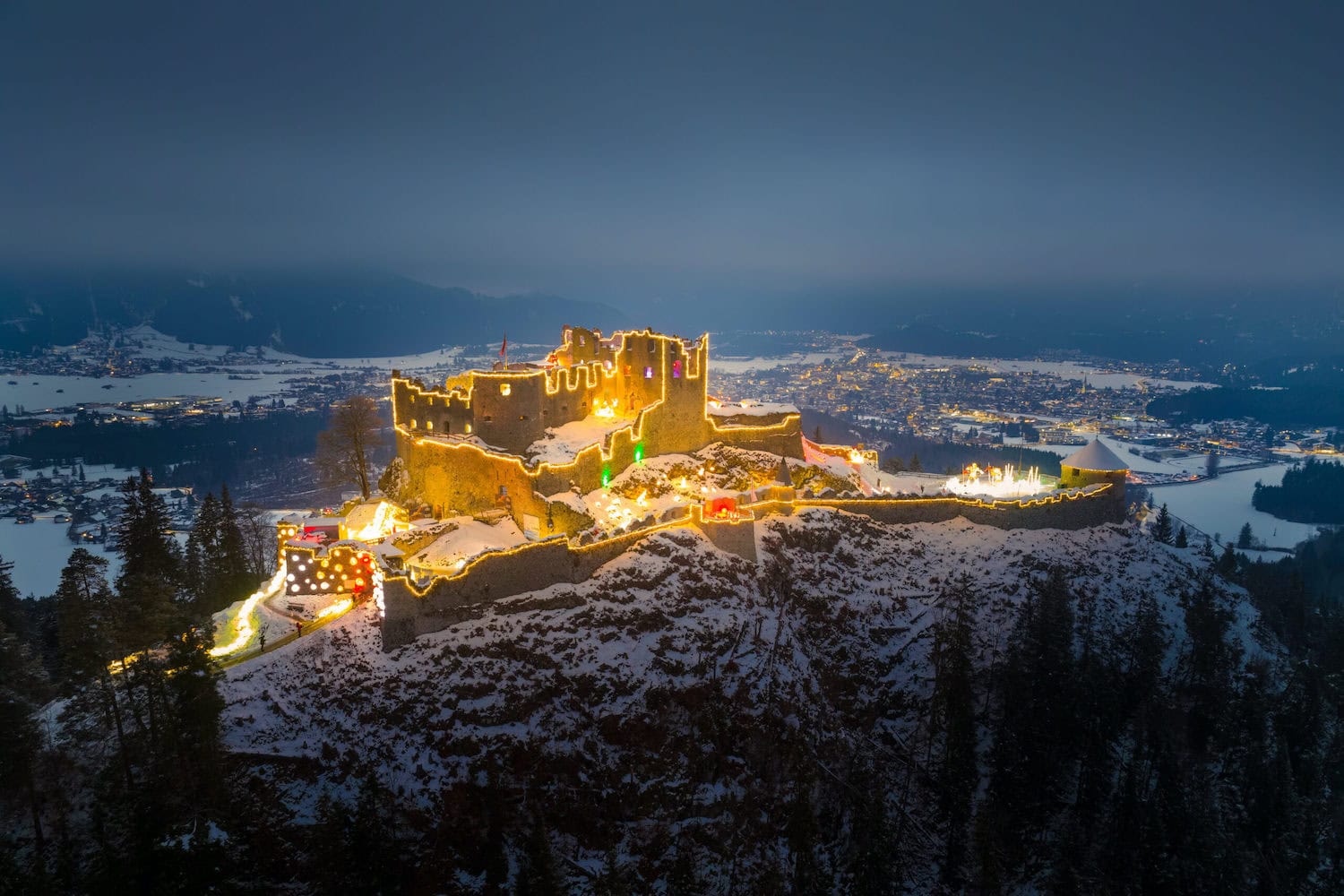 Mit vielen Lichtern angestrahlte Burgruine auf einem verschneiten Berg der Lumagica Route