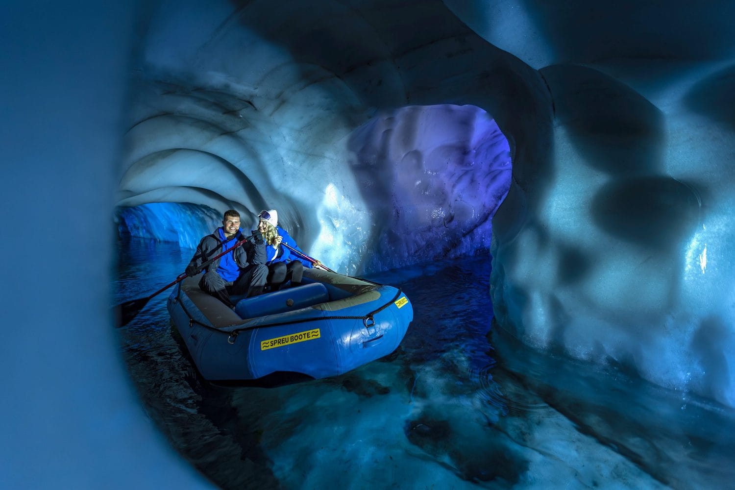 Zwei Menschen in einem Gummiboot durch einen wie mit blauen Nordlichtern angeleuchteten Gletscherfluss in Hintertux
