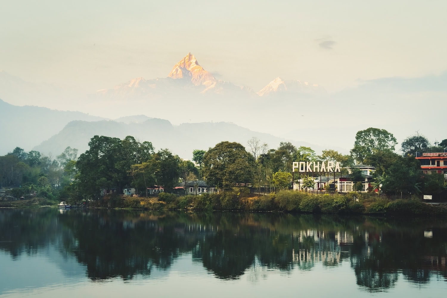 Pokhara City in Nepal vor dem Phewa Lake. Am Ufer ist der Schriftzug Pokhara zu sehen, im Hintergrund taucht aus dem Nebel das Annapurna Massiv auf.
