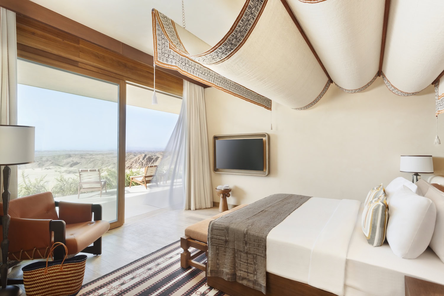 Six Senses Southern Dunes, Zimmer in hellen Farben mit arabischen Akzenten als Betthimmel und großem Fenster mit Blick zur Wüste