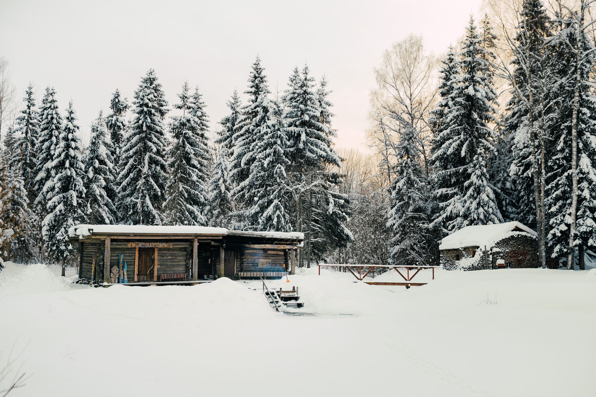 Sauna inmitten einer verschneiten Landschaft mit scheebedeckten Nadelbäumen.