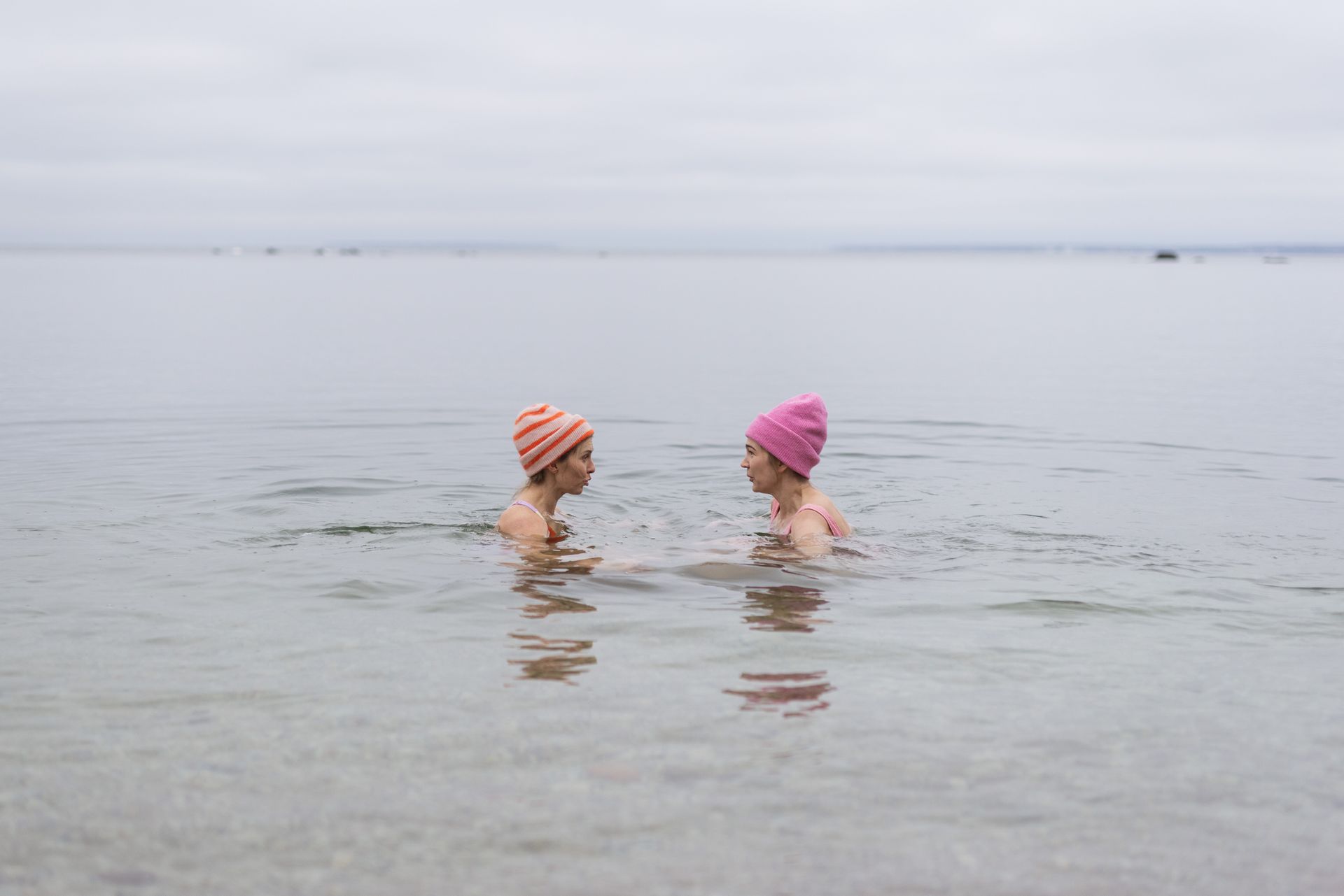 Zwei Frauen im Wasser mit Strickmützen beim Winterschwimmen.