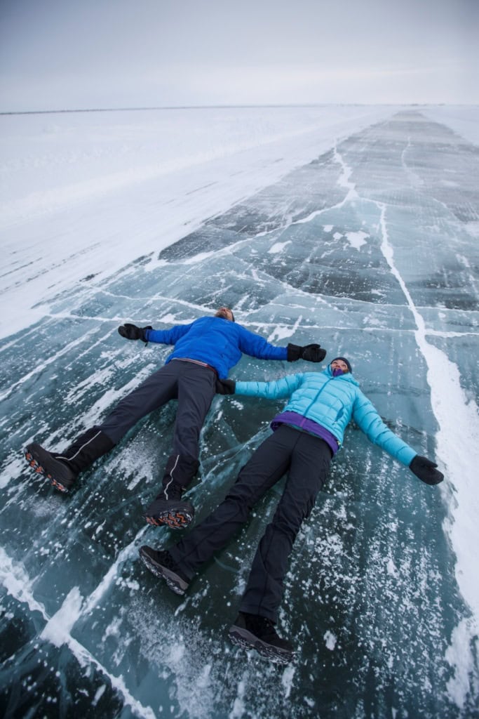 Zwei Personen in Funktionskleidung liegen auf einer Iceroad in Kanada.