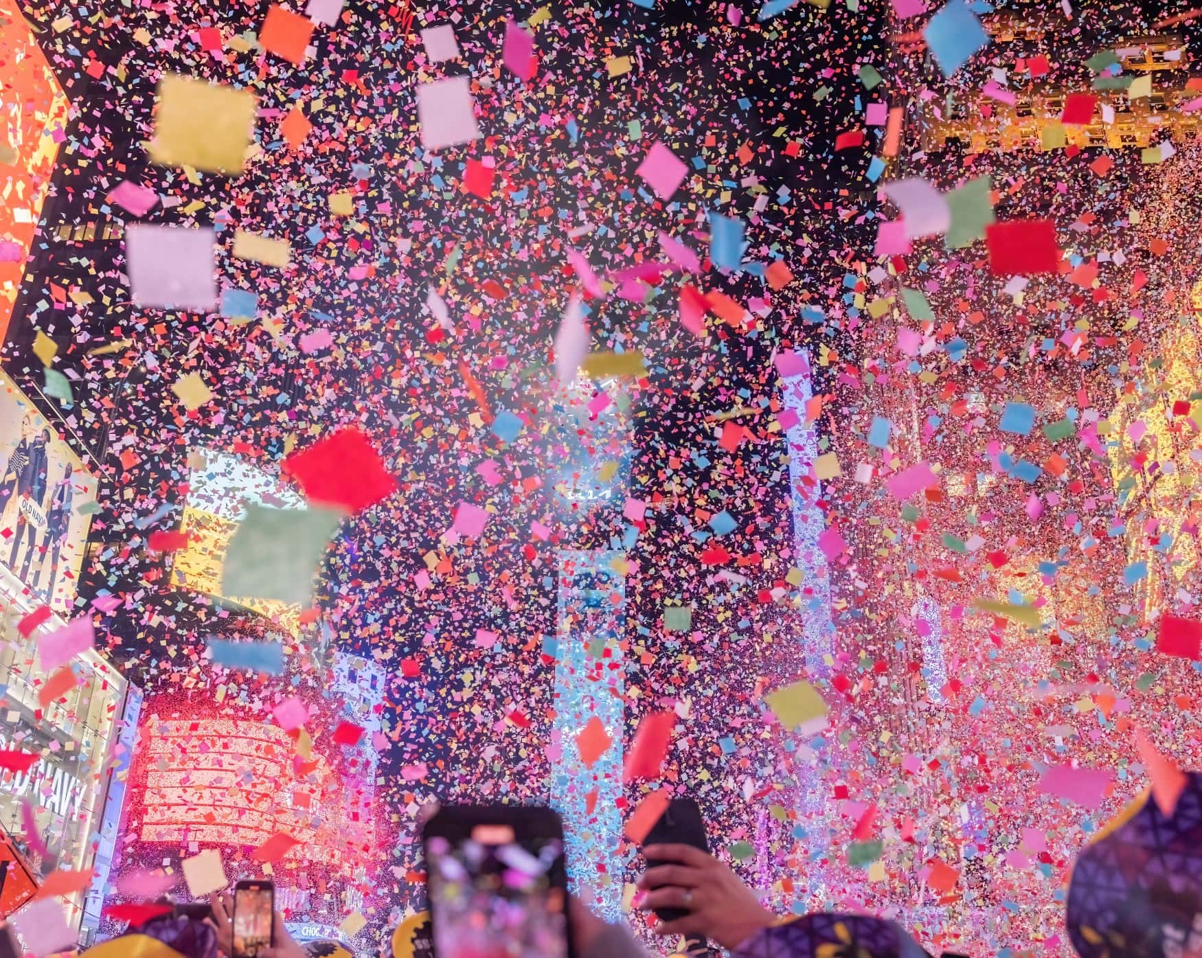Silvesterfeier auf dem Times Square in New York; dichtes Konfetti regnet vom Himmel, durch das noch der Times Square One zu sehen ist.