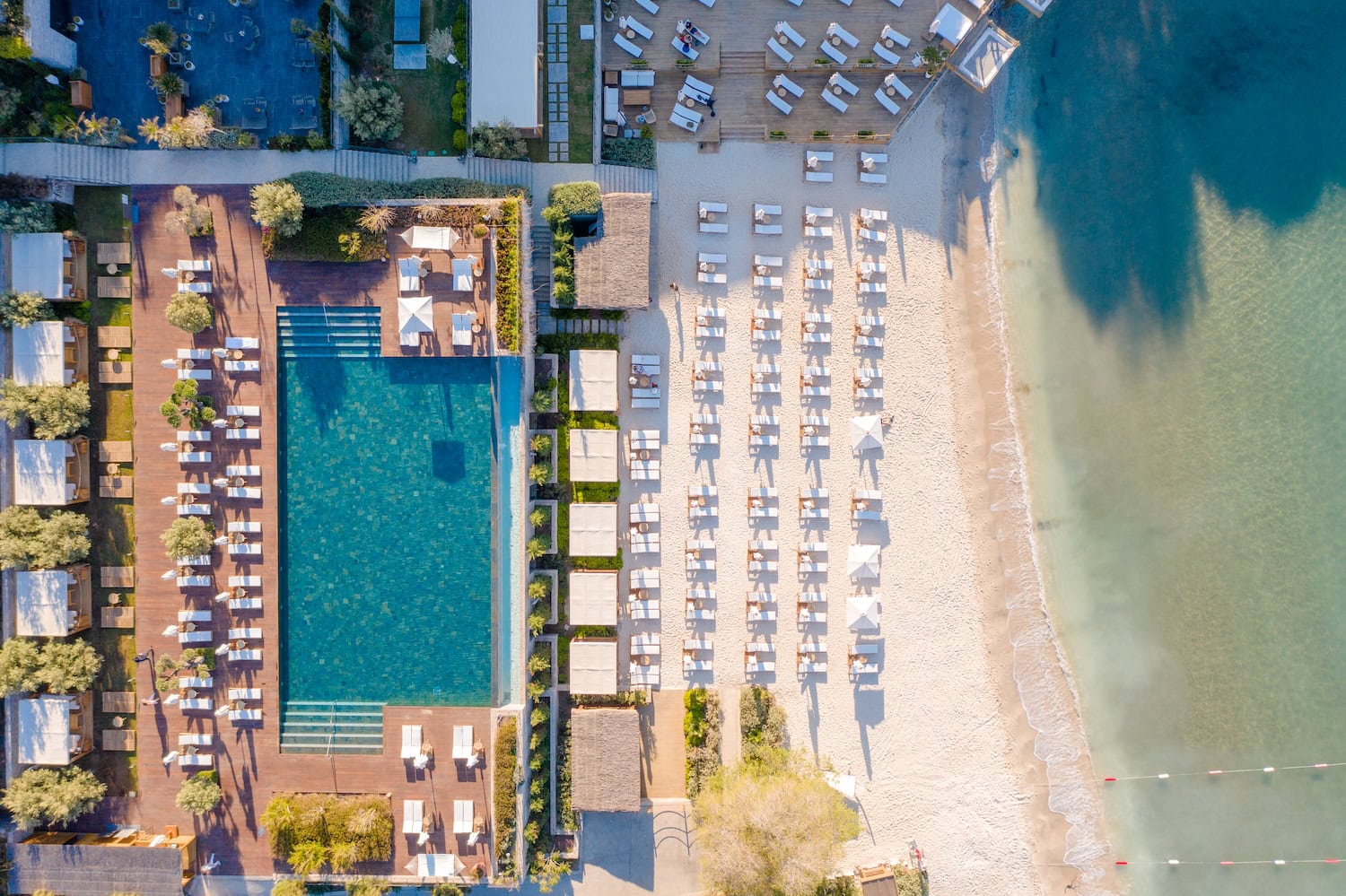 Luftbild auf Ferienanlage in Bodrum, weißer Sandstrand am türkisen Meer, Liegestühle und ein großer Pool