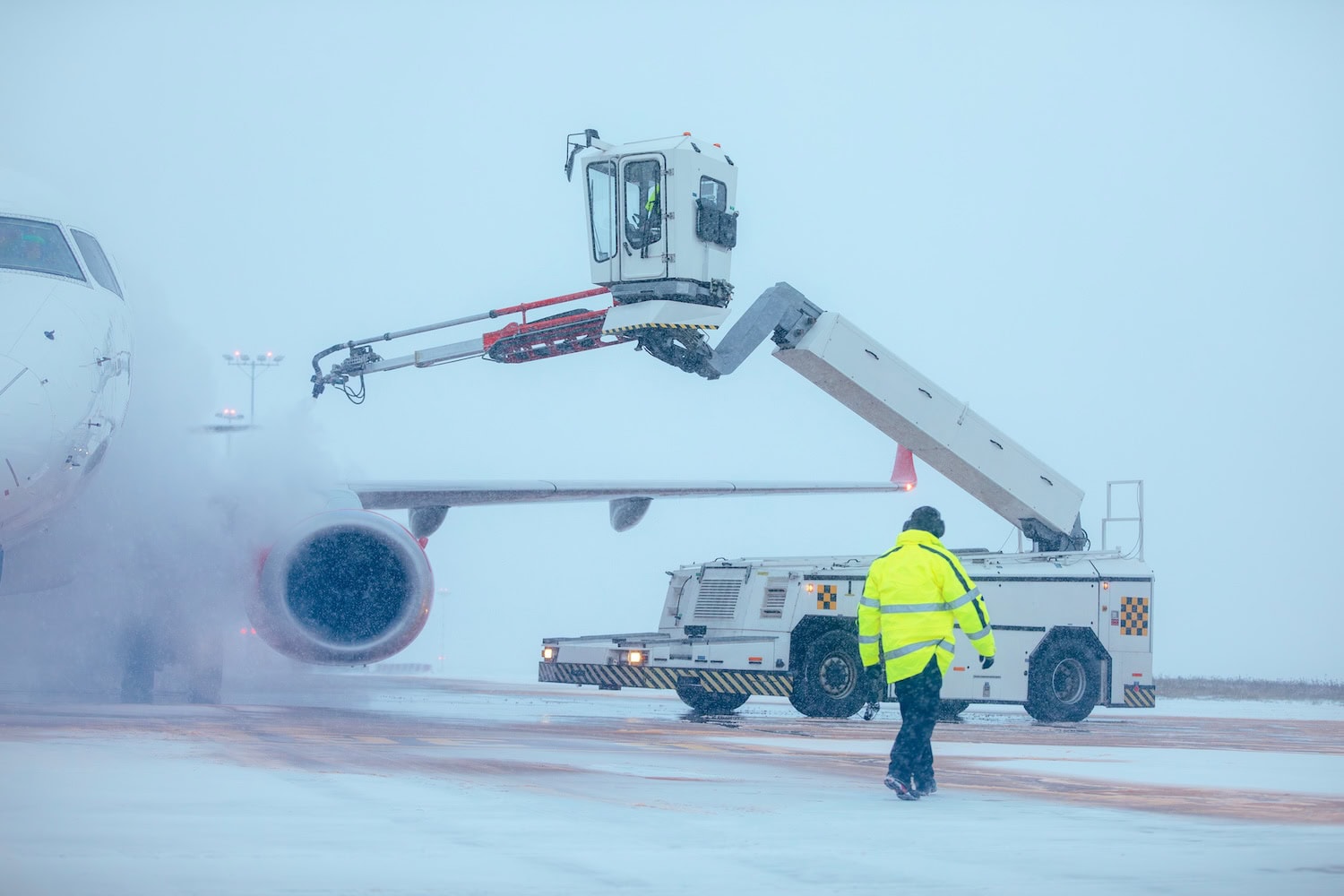 Flugzeug wird enteist, im Vordergrund Mann mit Sicherheitsjacke