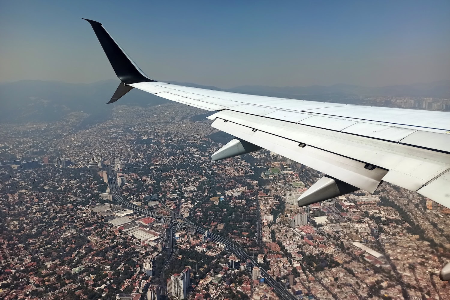 Flugzeug über Mexico City, auf der rechten Seite sieht man den Flugzeugflügel, darunter die Stadt mit ihren unzähligen Gebäuden und Straßen.