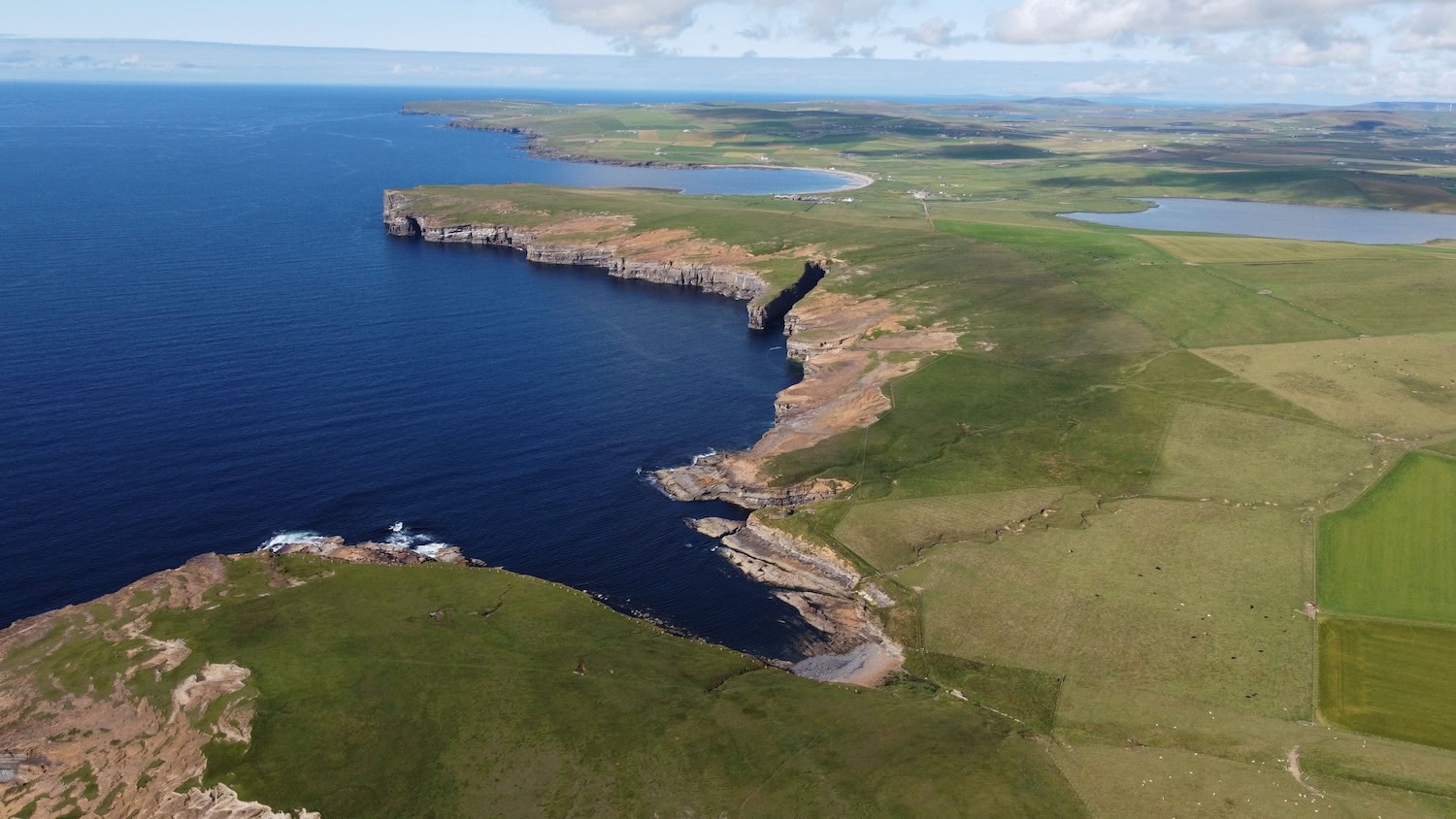 Luftaufnahme der Orkney Inseln in Schottland, blaues Meer, Steilküsten und grüne Wiesen.