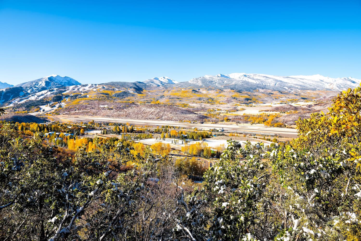 Pitkin County Airport, Colorado: im Hintergrund die schneebedeckten Berge der Rocky Mountains, in der Mitte die Landebahn, alles umgeben von rauher Natur.