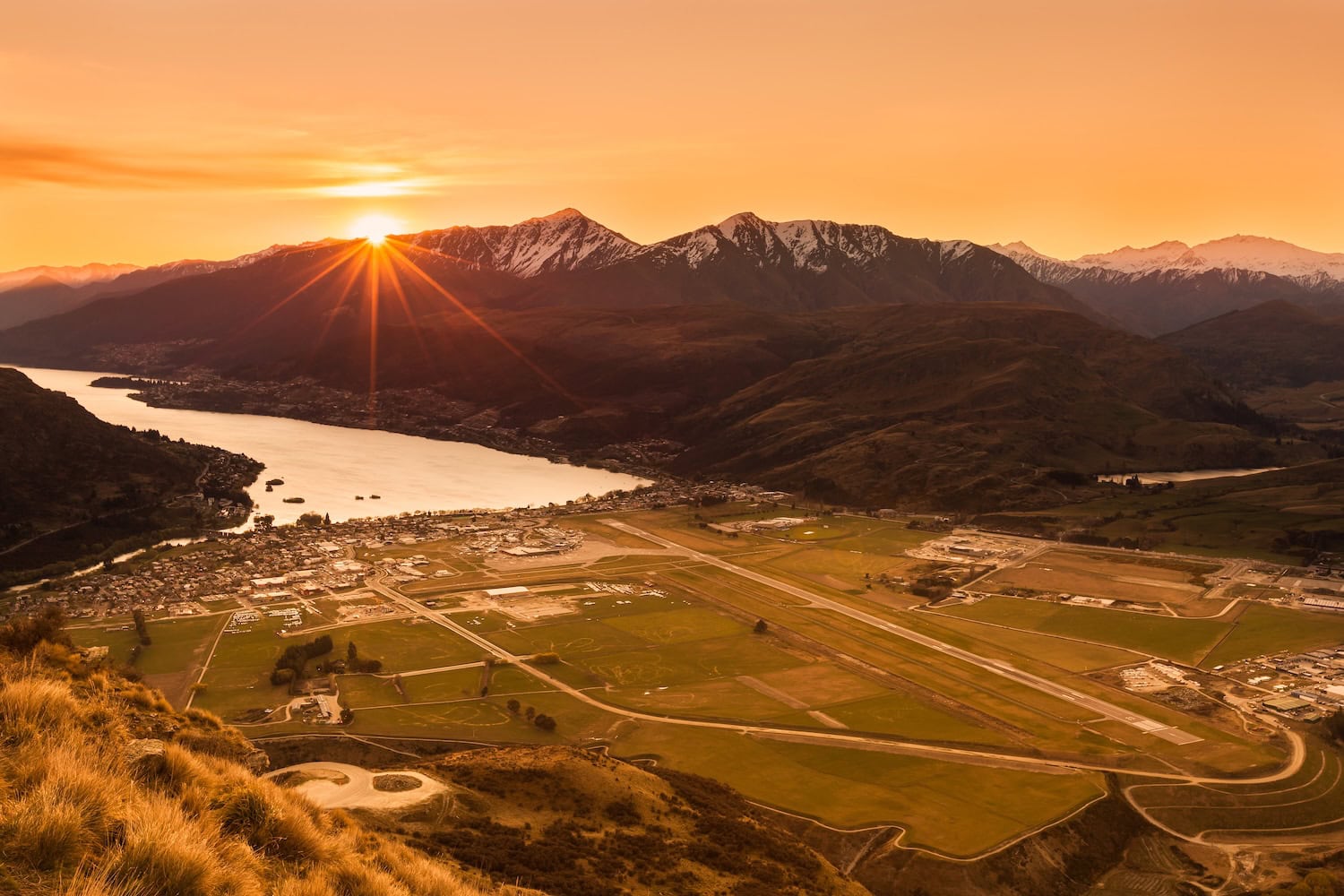 Flughafen Queenstown in Neuseeland zum Sonnenuntergang. Eine Landebahn, vor einem Fjord inmitten von Bergen im orangen Licht.