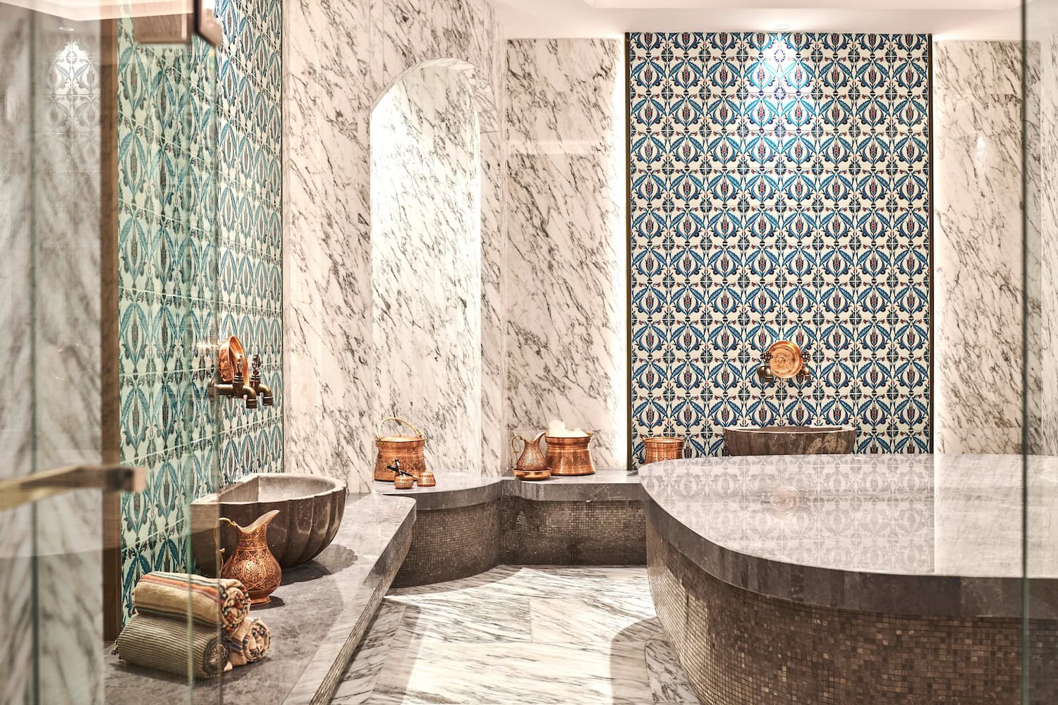 Traditioneller türkischer Hamam, mit Marmor und blau gemusterten Fliesen, in der Mitte der Mamorblock, an den Seiten die Utensilien zum Baden.