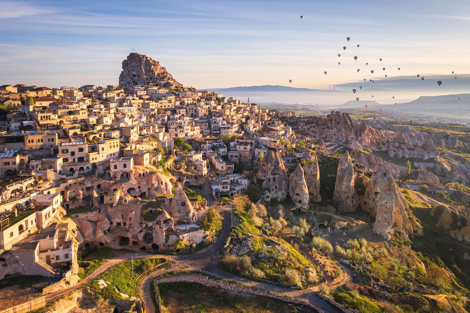 Uchisar in Kappadokien: ein Dorf auf einem hohen Felsen mit Ausblick über die Landschaft und den berühmten Ballons darüber.