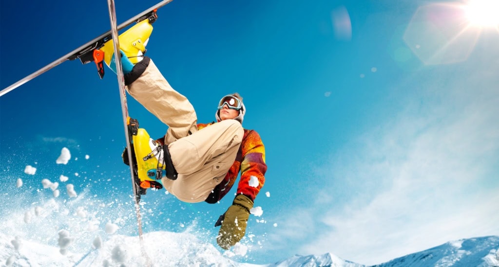Mensch springt mit bunter Skikleidung vor blauem Himmel