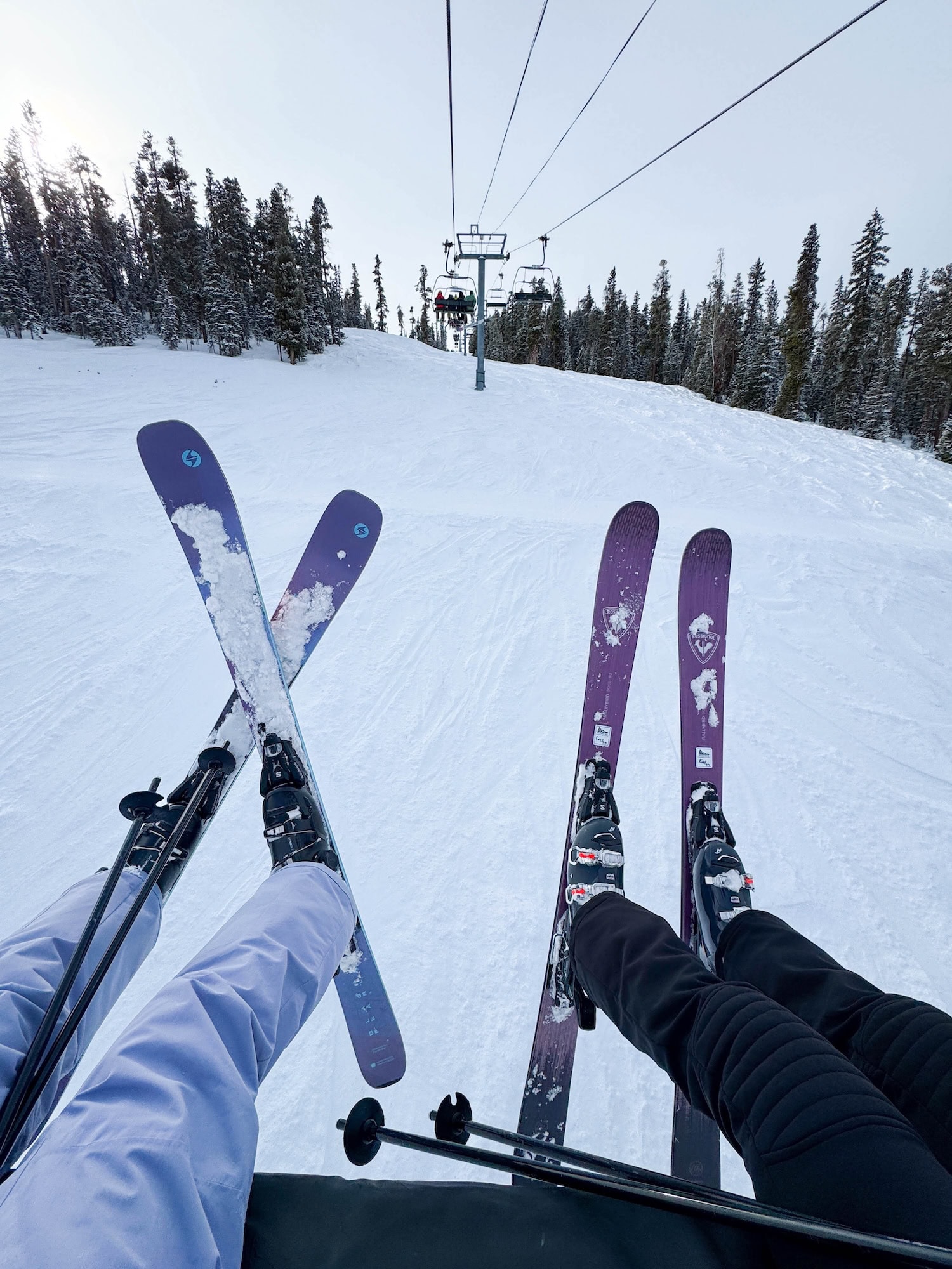 zwei Menschen mit Skiern auf einem Lift in den Bergen