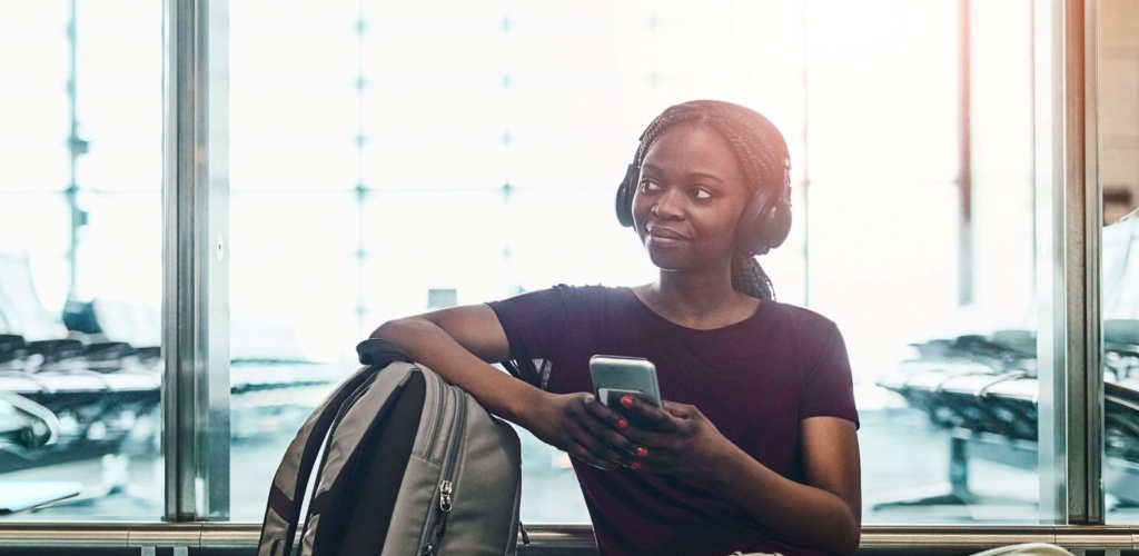 Junge Frau sitzt auf Boden im Flughafen mit Handy in der Hand