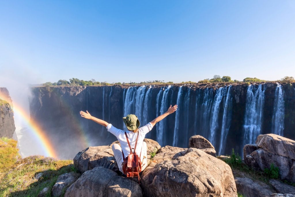 Grenzerlebnisse weltweit: Eine Frau sitzt auf Felsen vor den Victoria Wasserfällen in Simbabwe