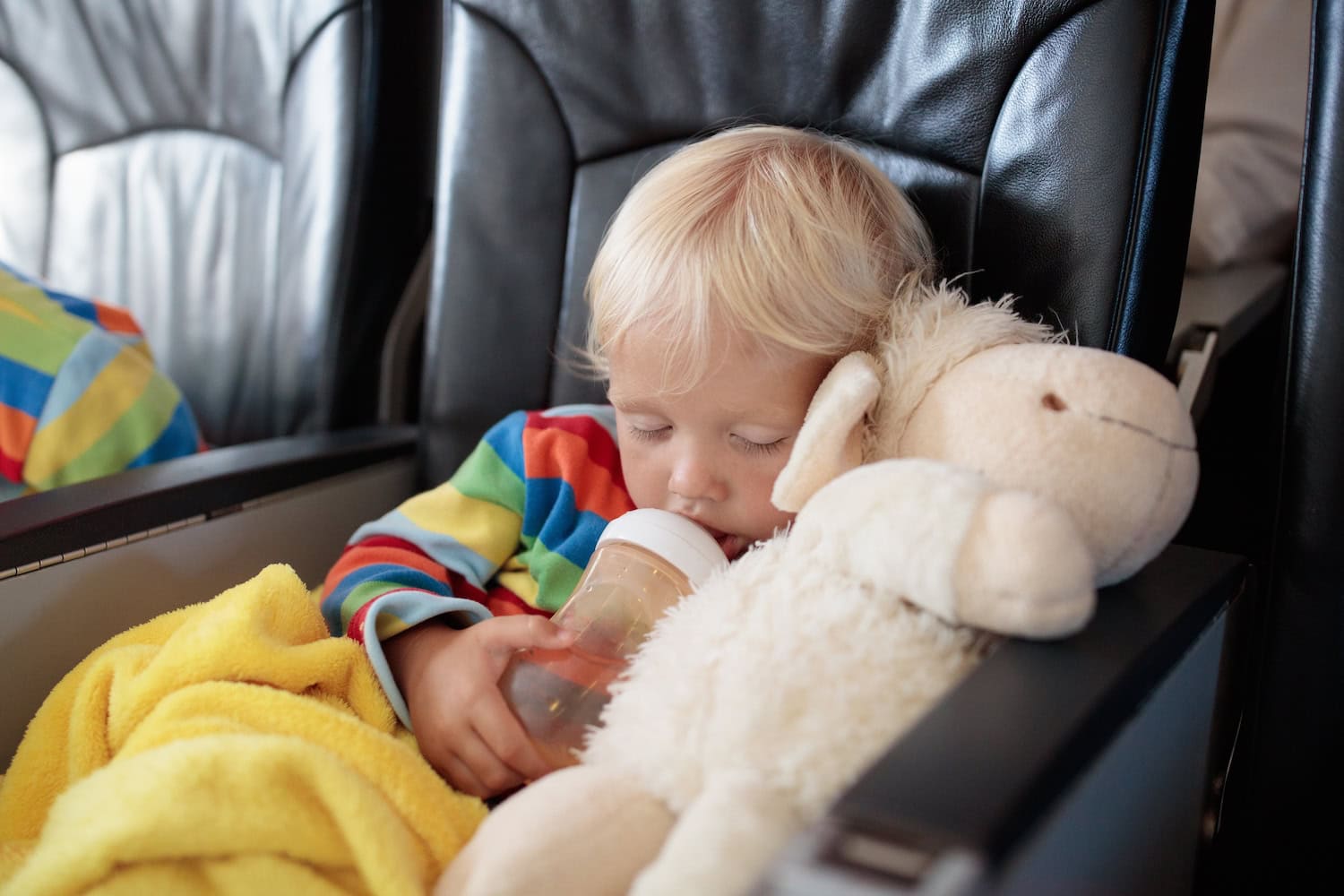 Fliegen mit Baby und Kleinkind Tipps: Schlafendes Kind im Flugzeug mit Flasche und Kuscheltier