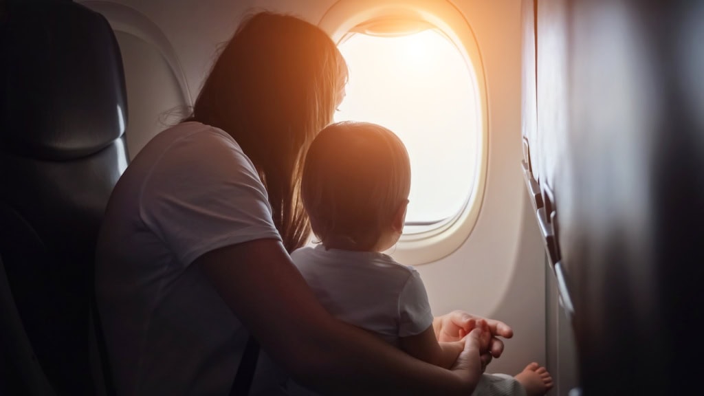 Mutter mit Kleinkind im Flugzeug im Abendlicht: Fliegen mit Baby und Kleinkind Tipps