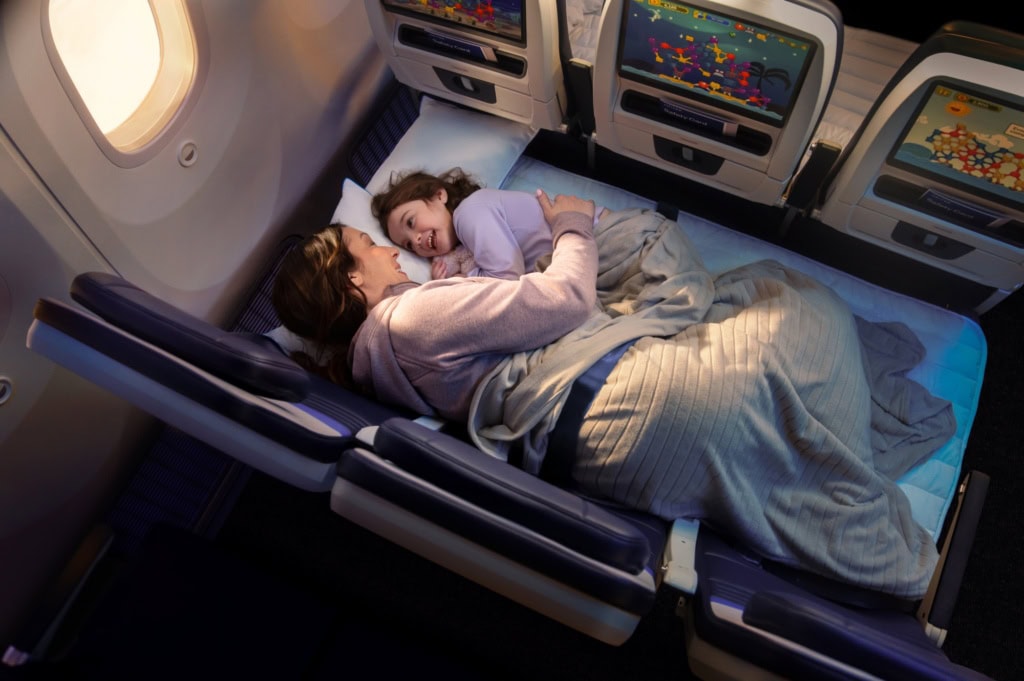 Eine Mutter und ein Kind liegen in einem Flugzeug auf einer zu einer Liegefläche umfunktionierten Dreiersitzreihe.