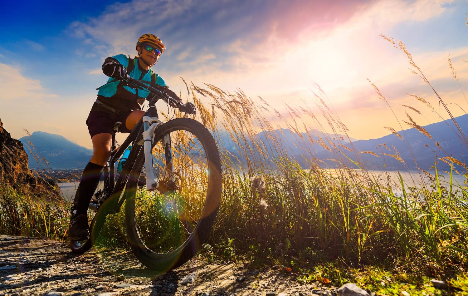 Frau auf Mountainbike am Gardasee bei dramatischen Himmel im Sommer. Im Hintergrund die Berge und der See, das Foto wurde von unten geschossen.