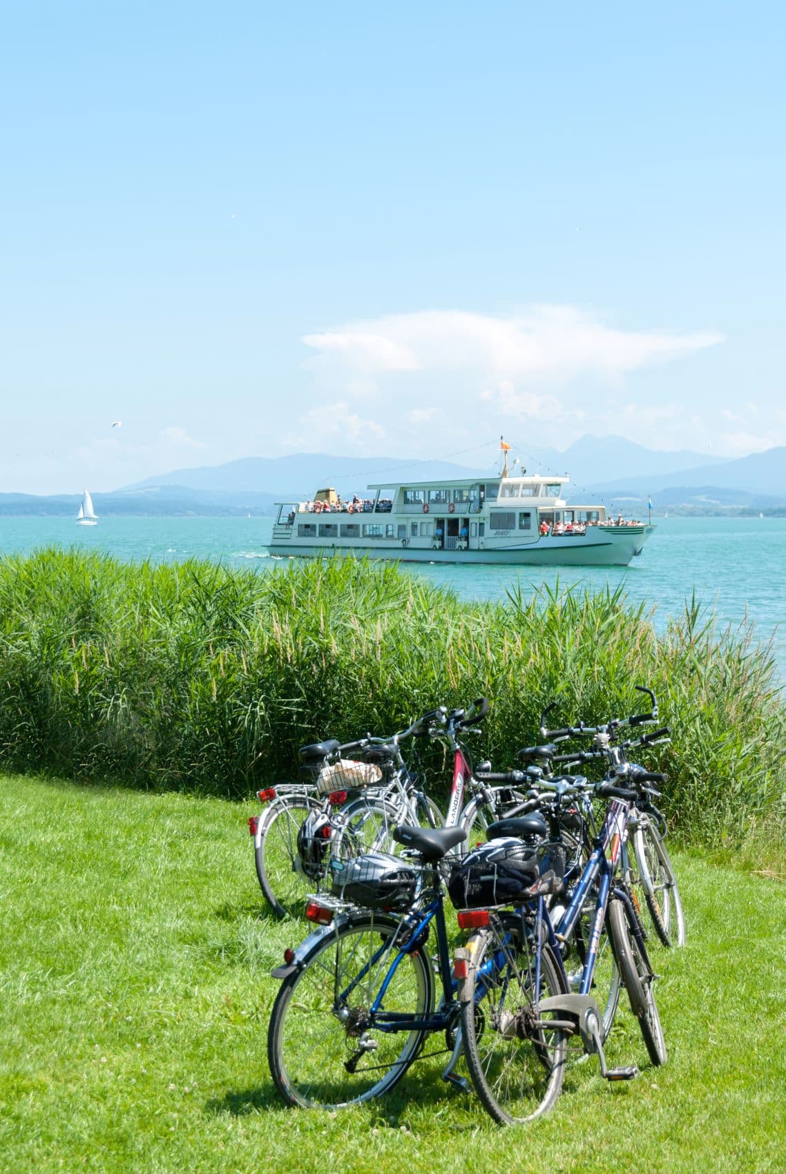 Mehrere Fahrräder stehen auf einer Wiese am Chiemsee, im Hintergrund ein Schiff 