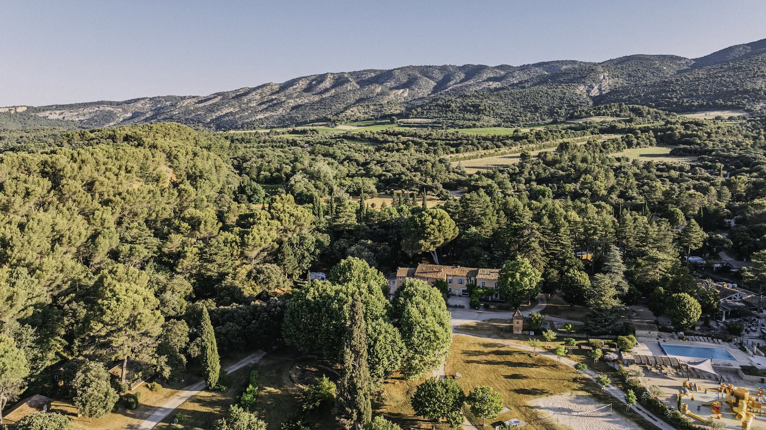Luftbild des Campingplatzes Belezy in Frankreich: inmitten von dicht bewachsenen Hügeln liegt ein französisches Landhaus und eine Pool-Area.