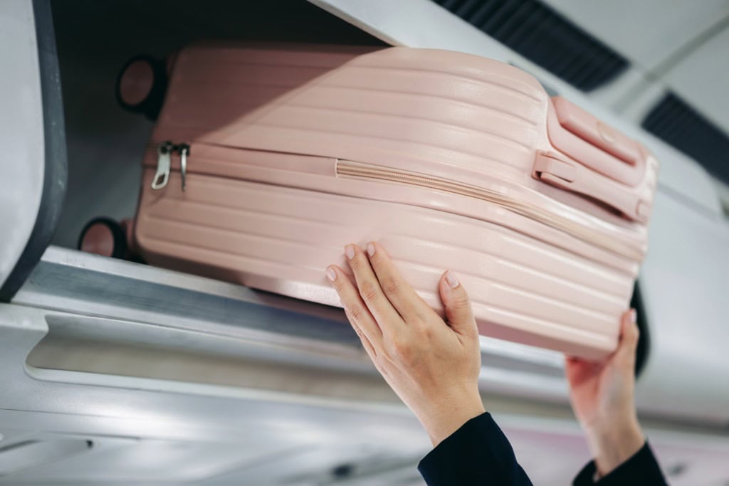 Eine Frau hebt einen Koffer in die Ablage im Flugzeug.