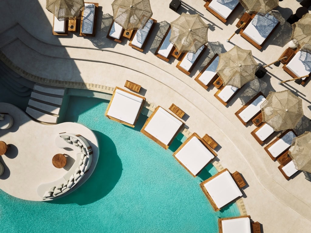 Luftaufnahme eines geschwungenen Pools in einem Resort auf Zypern. Am Rand ragen einige breite Liegen über die Wasseroberfläche.