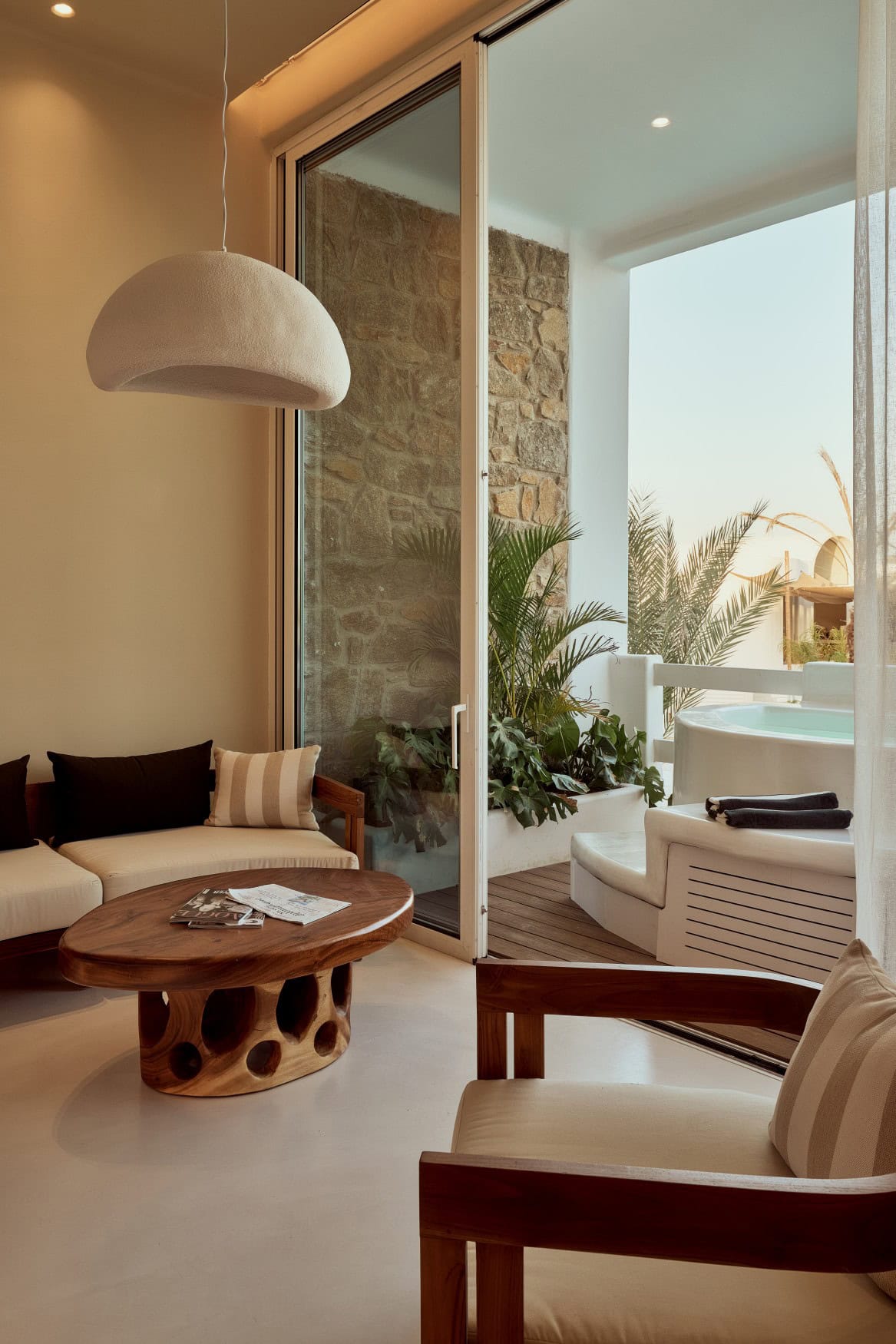 Sitzecke in einem griechischen Resort, mit modernem Stil. Durch eine gläserne Tür geht es auf den Balkon, auf dem ein kleiner Whirpool steht.