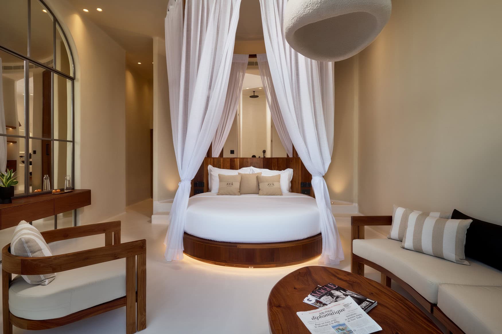 Ein Zimmer in einem mediterranen Resort; im Zentrum ein rundes, großes Bett, überdacht von einem weißen Baldachin.
