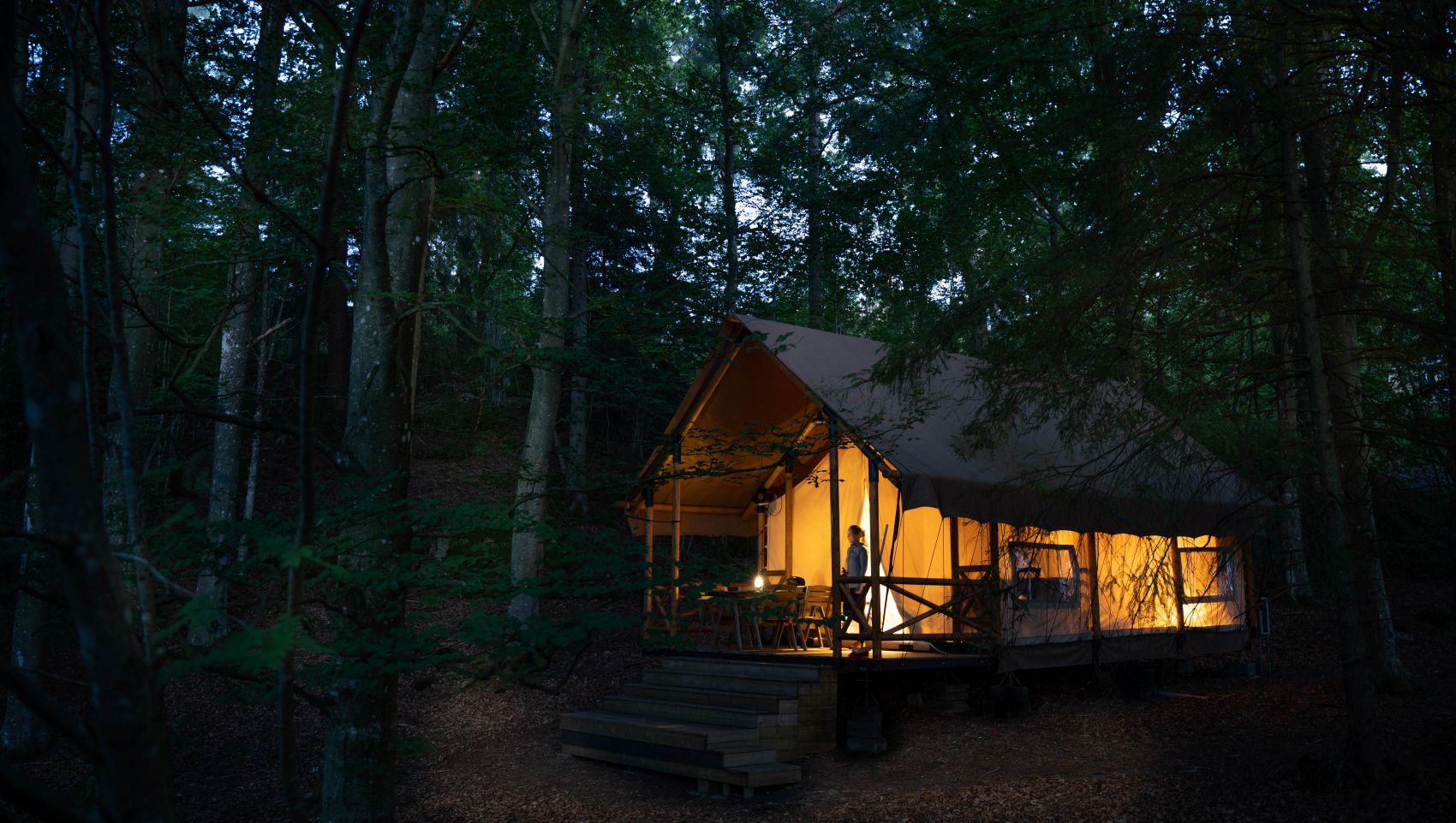 Beleuchtetes Glamping-Zelt mitten im Wald von Westschweden bei Abenddämmerung – naturnahes Übernachten in ruhiger Atmosphäre.
