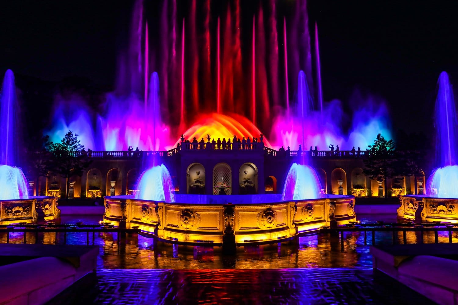 Spektakuläre Fontänen-Lichtshow in Longwood Gardens bei Nacht in Pink, Blau und Gelb über beleuchteter Sandstein-Balustrade