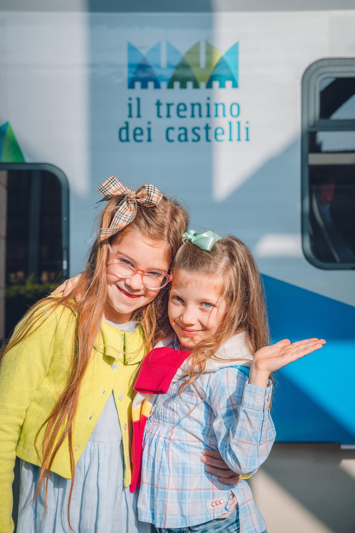 Zwei Mädchen vor dem Zug Il Trenino dei Castelli, die dem Zuschauer zuwinken.