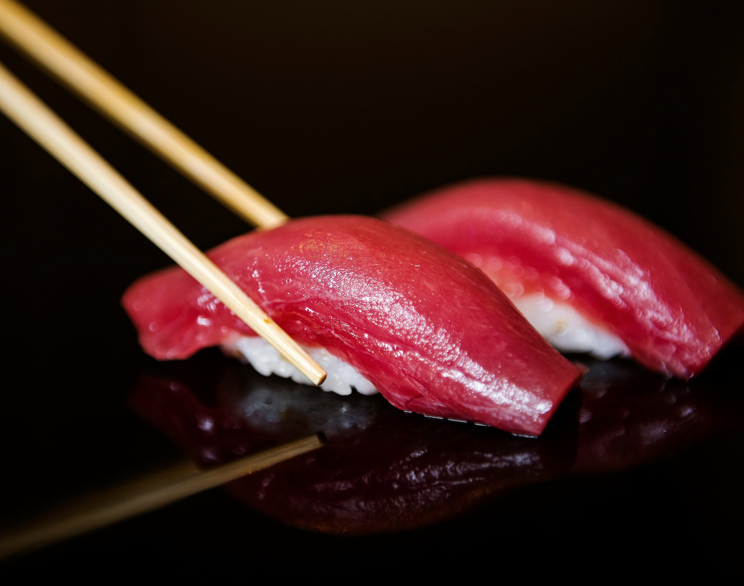 Ein Thunfisch Nigiri auf schwarz mit Stäbchen
